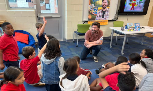 Male author sits and talks with fifth grade students in the media center